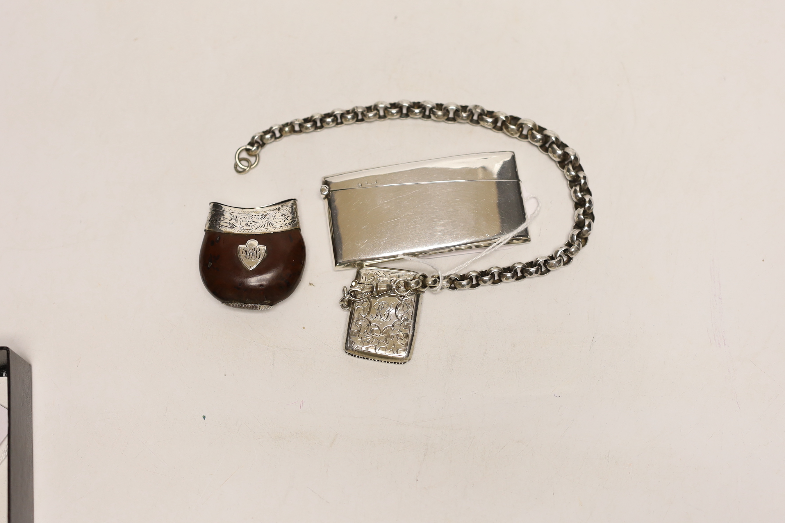 An Edwardian silver vesta case on a white metal belcher link chain, a 19th century white metal mounted nut vesta case and a George V silver card case, 83mm.